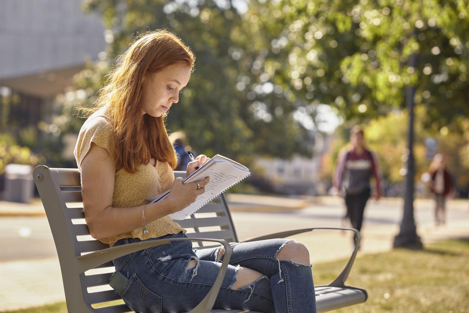 A <a href='http://fzqo.uni-foodex.com'>BETVLCTOR伟德登录</a> student reads on a bench along Campus Drive.